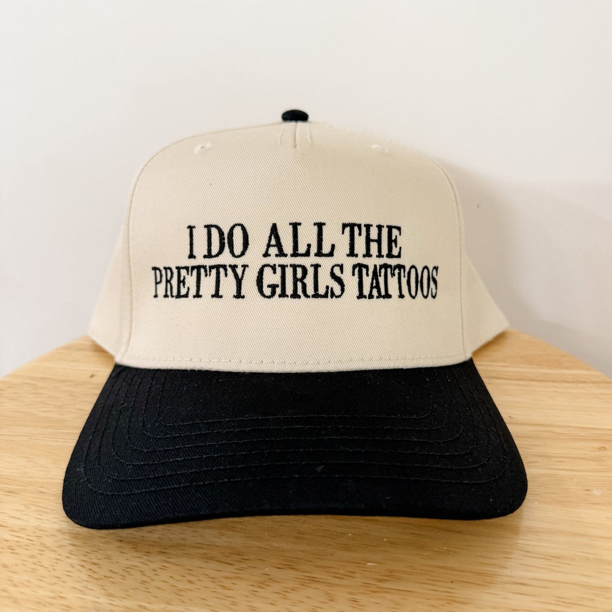 Cream and black trucker hat with front panel text: 'I DO ALL THE PRETTY GIRLS TATTOOS'