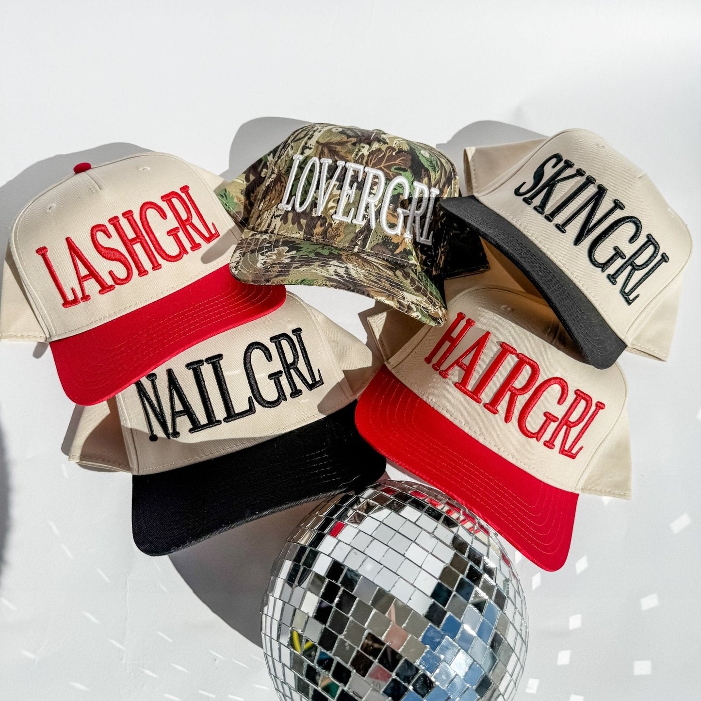 Assorted trucker hats with cream panels, red brims, and embroidered slogans
