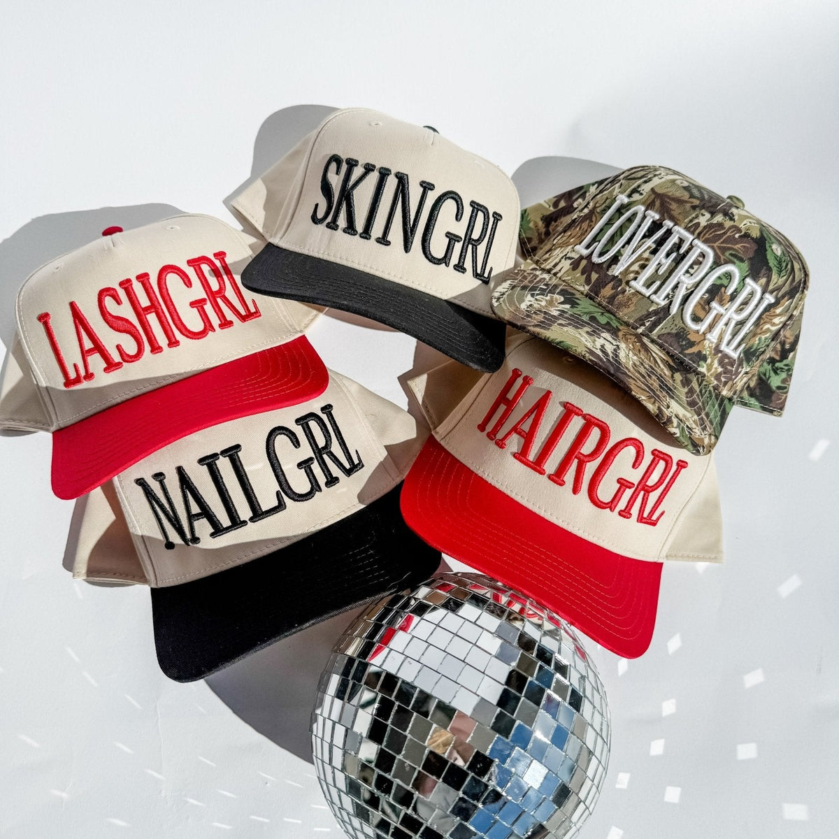 Assorted trucker hats with cream fronts, red and black brims, and camo panel with printed text