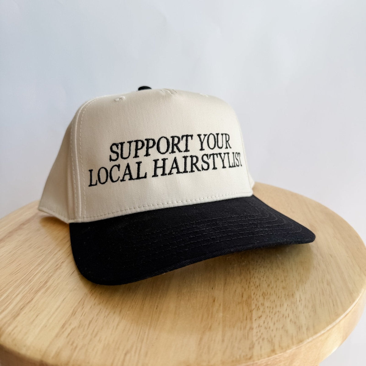 Cream front trucker hat with black brim and centered 'Support Your Local Hairstylist'