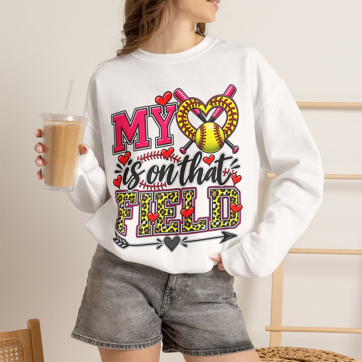 White crewneck sweatshirt worn with grey shorts; front shows “My Heart” softball graphic
