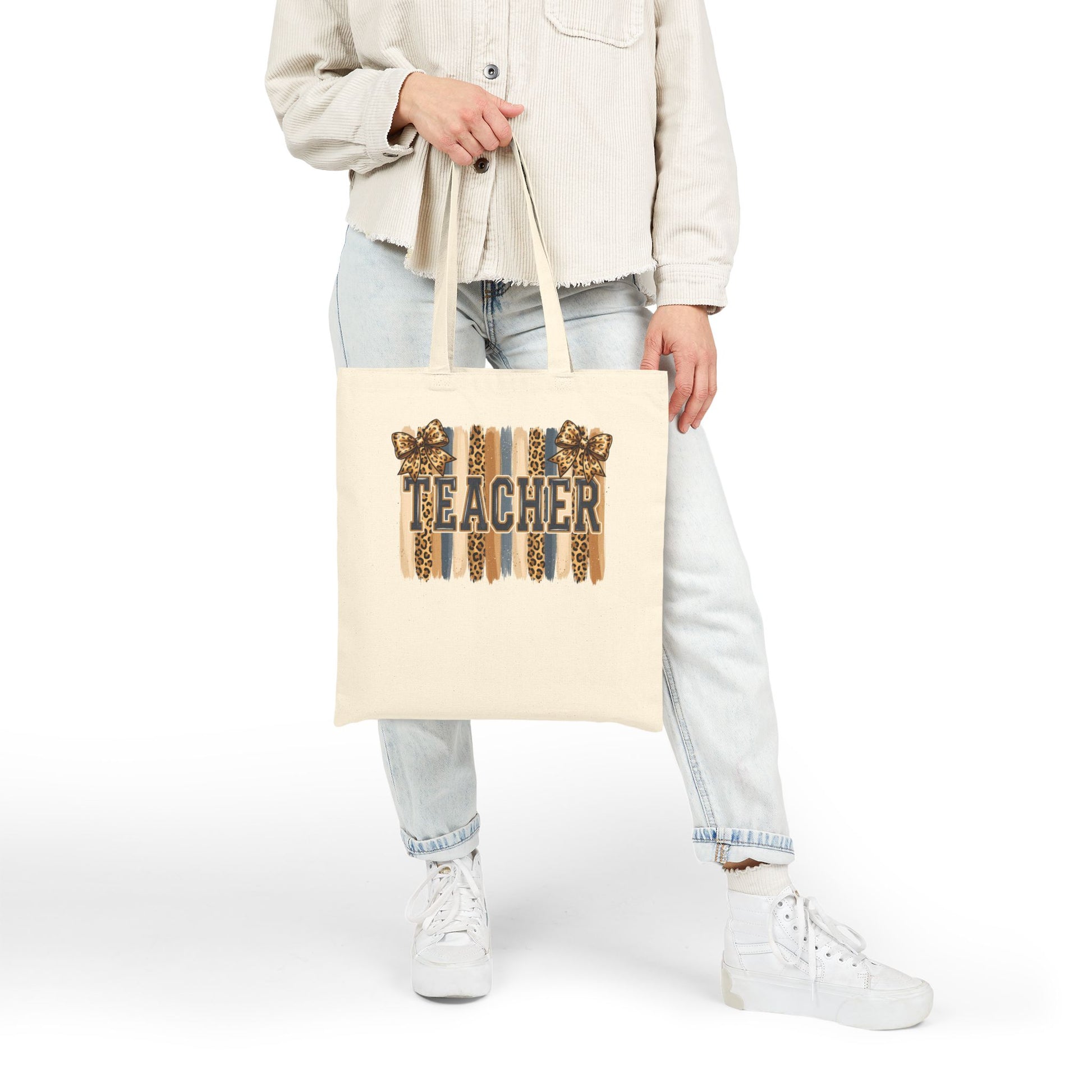 Natural canvas tote bag with leopard “Teacher” graphic, held at side