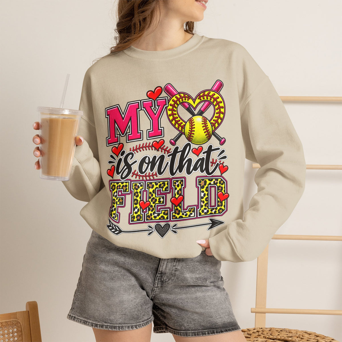 Sand crewneck sweatshirt worn with grey shorts; front shows hearts and softball graphic