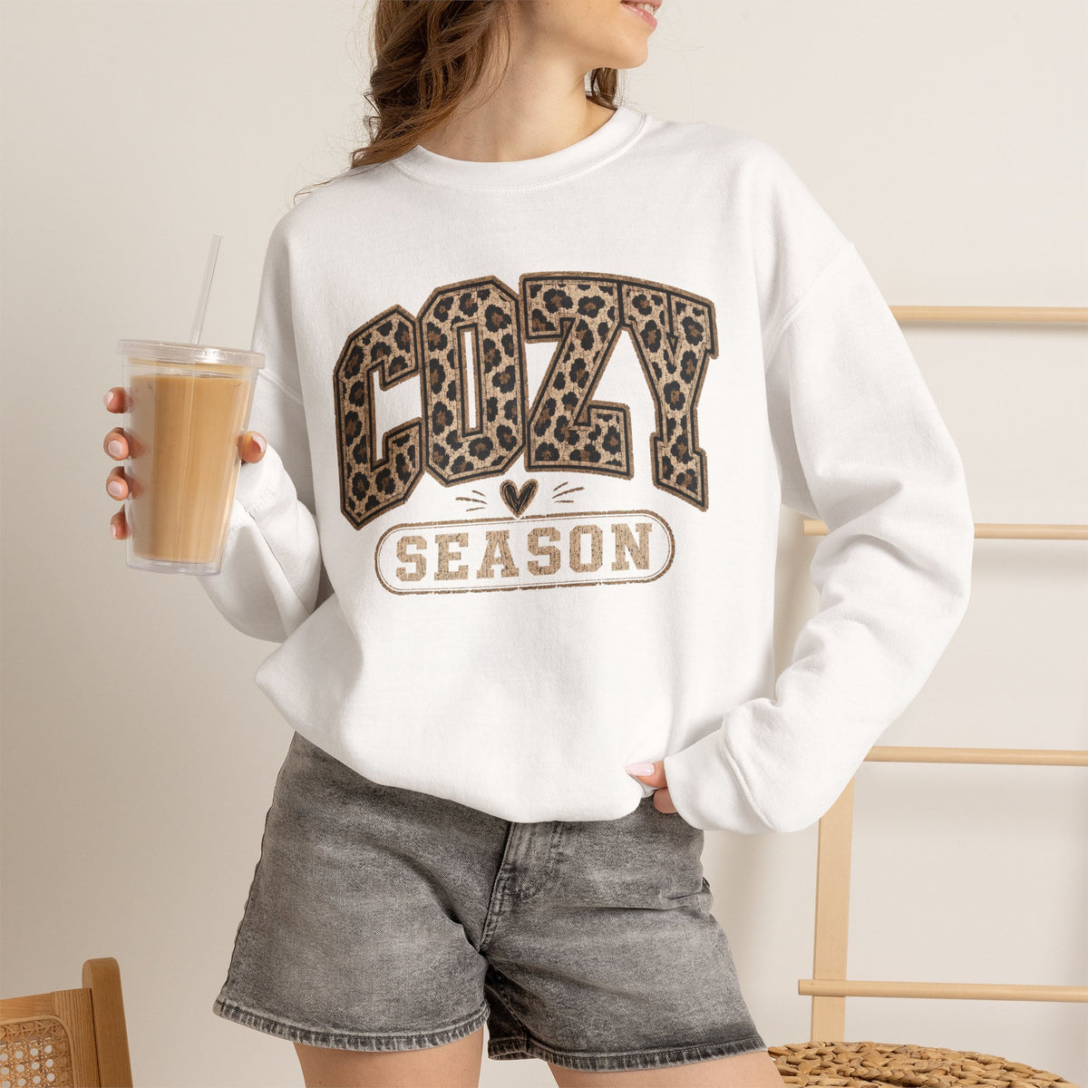 White crewneck sweatshirt worn with leopard-print “COZY” and “SEASON” front graphic