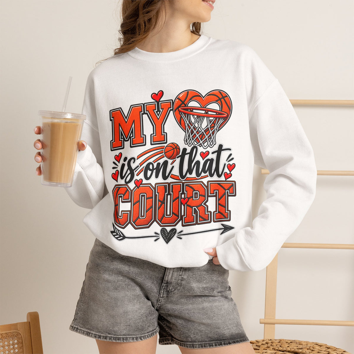 White crewneck sweatshirt with basketball heart graphic, worn with denim shorts