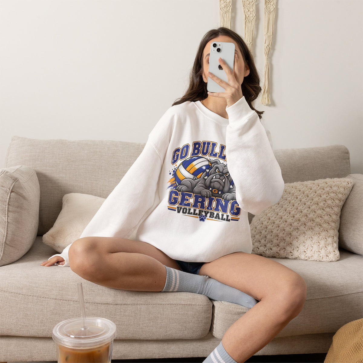 White crewneck sweatshirt worn by seated model, with bulldog and volleyball team graphic