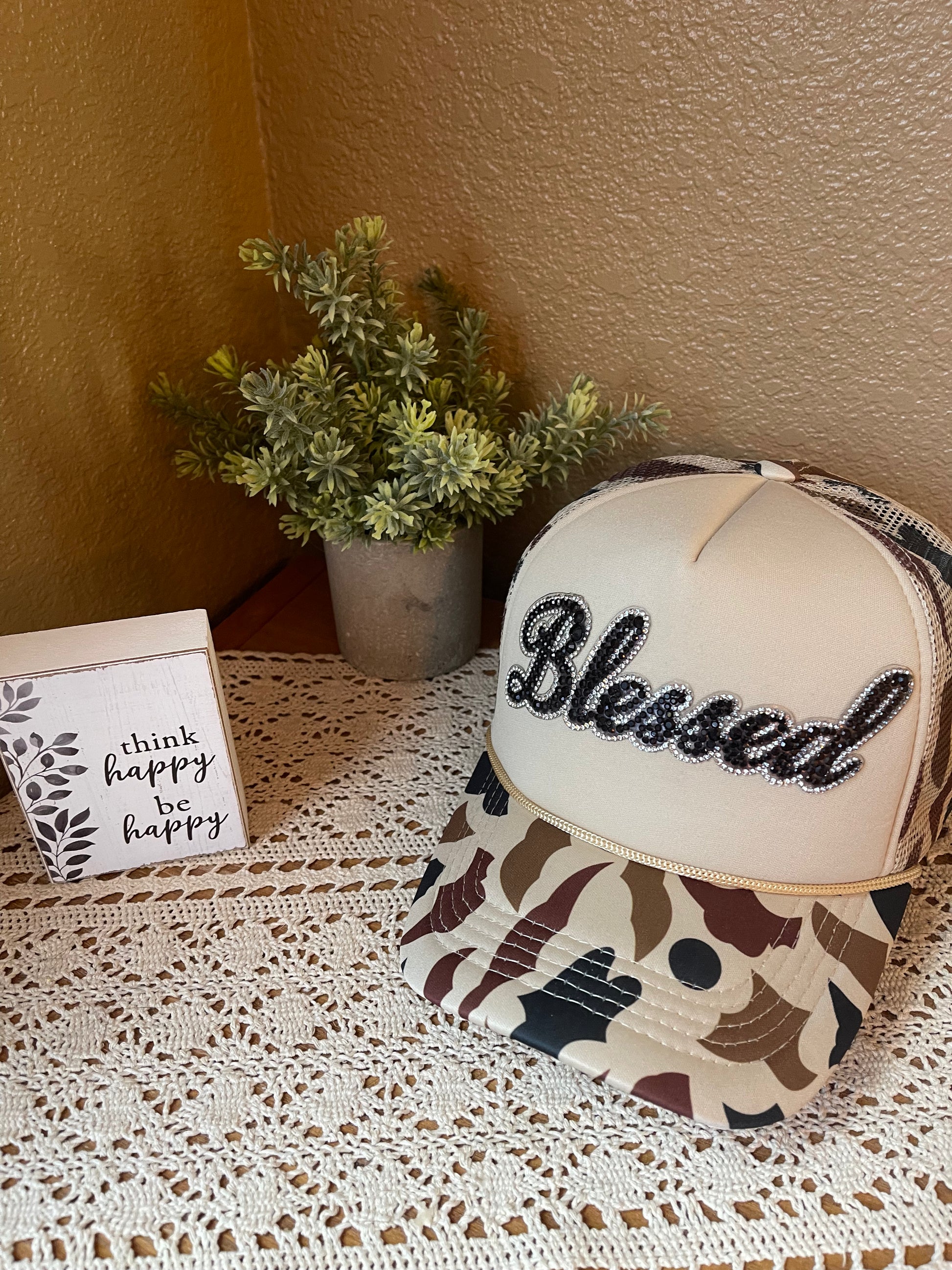 Camouflage trucker hat with beige mesh and black Blessed embroidery, curved brim