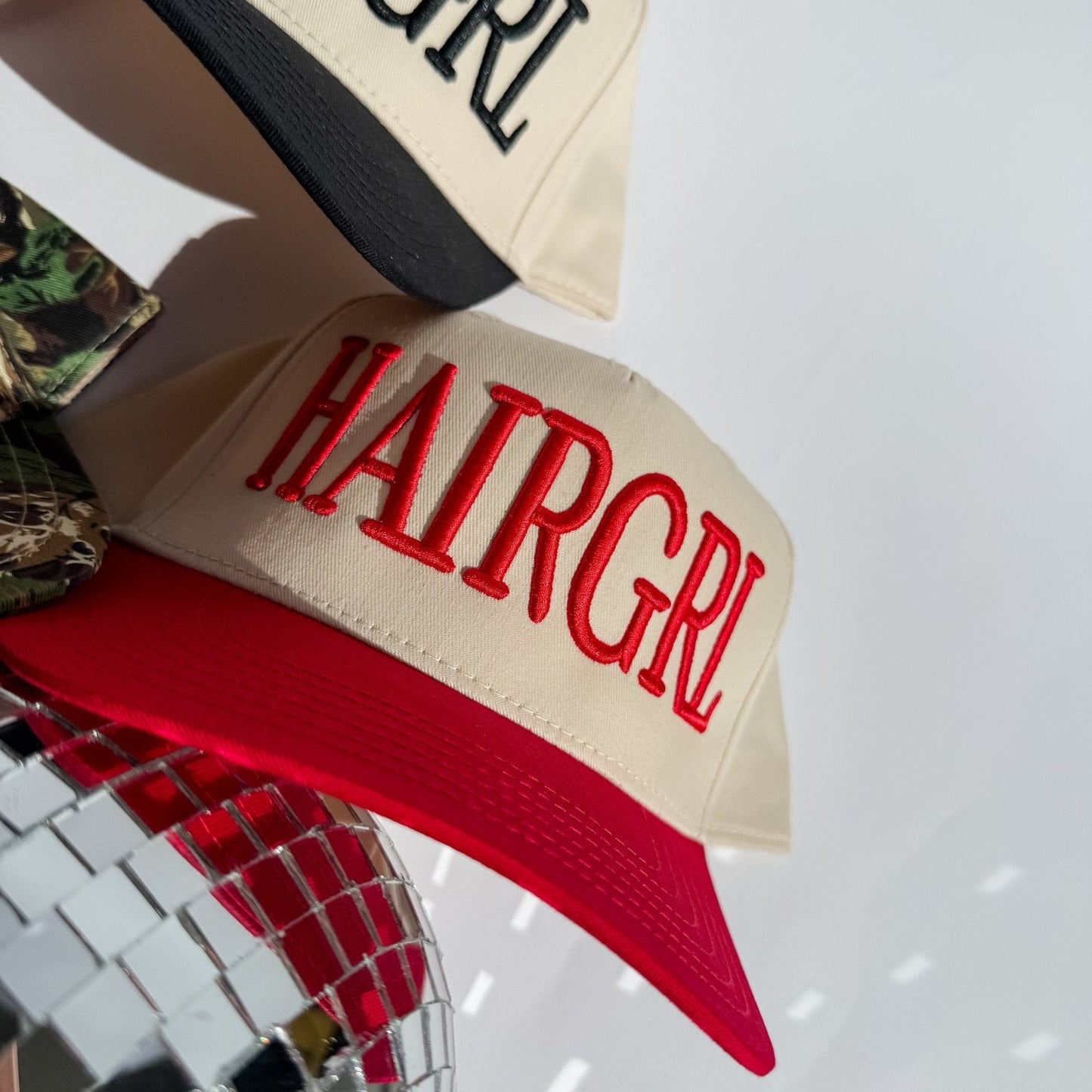 Cream HAIRGRL trucker hat with red front logo and red curved brim