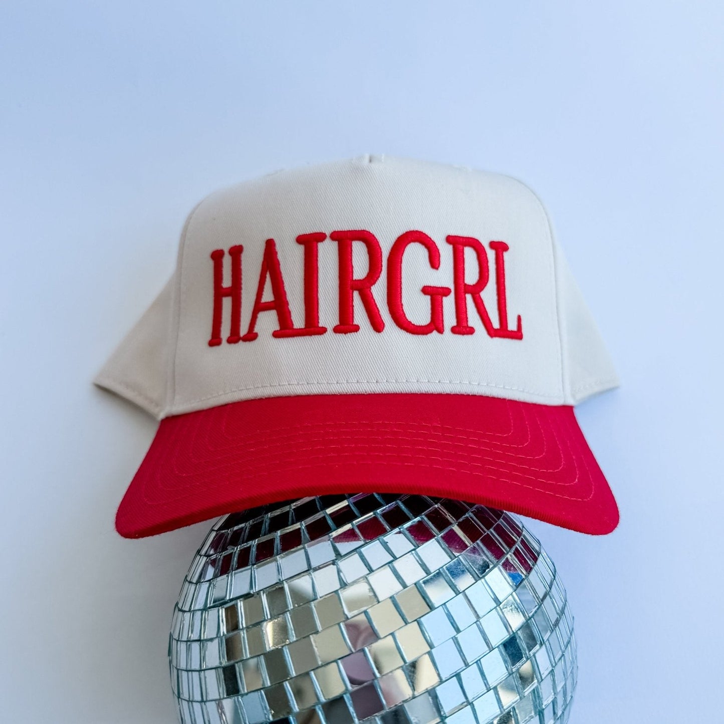 Cream and red HAIRGRL trucker hat with front logo and curved red brim