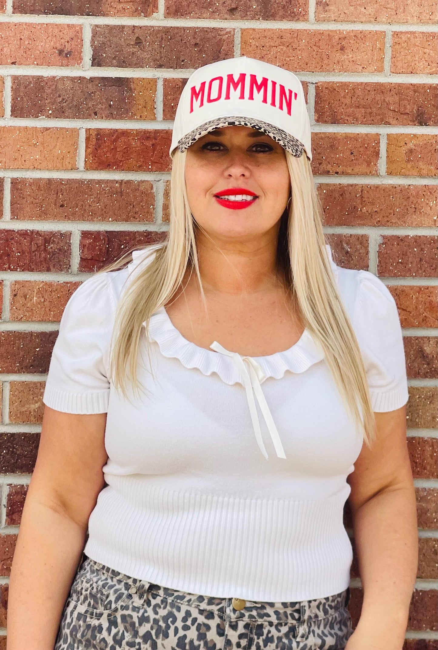 Mommin trucker hat on model: cream front with red MOMMIN and leopard-pattern brim