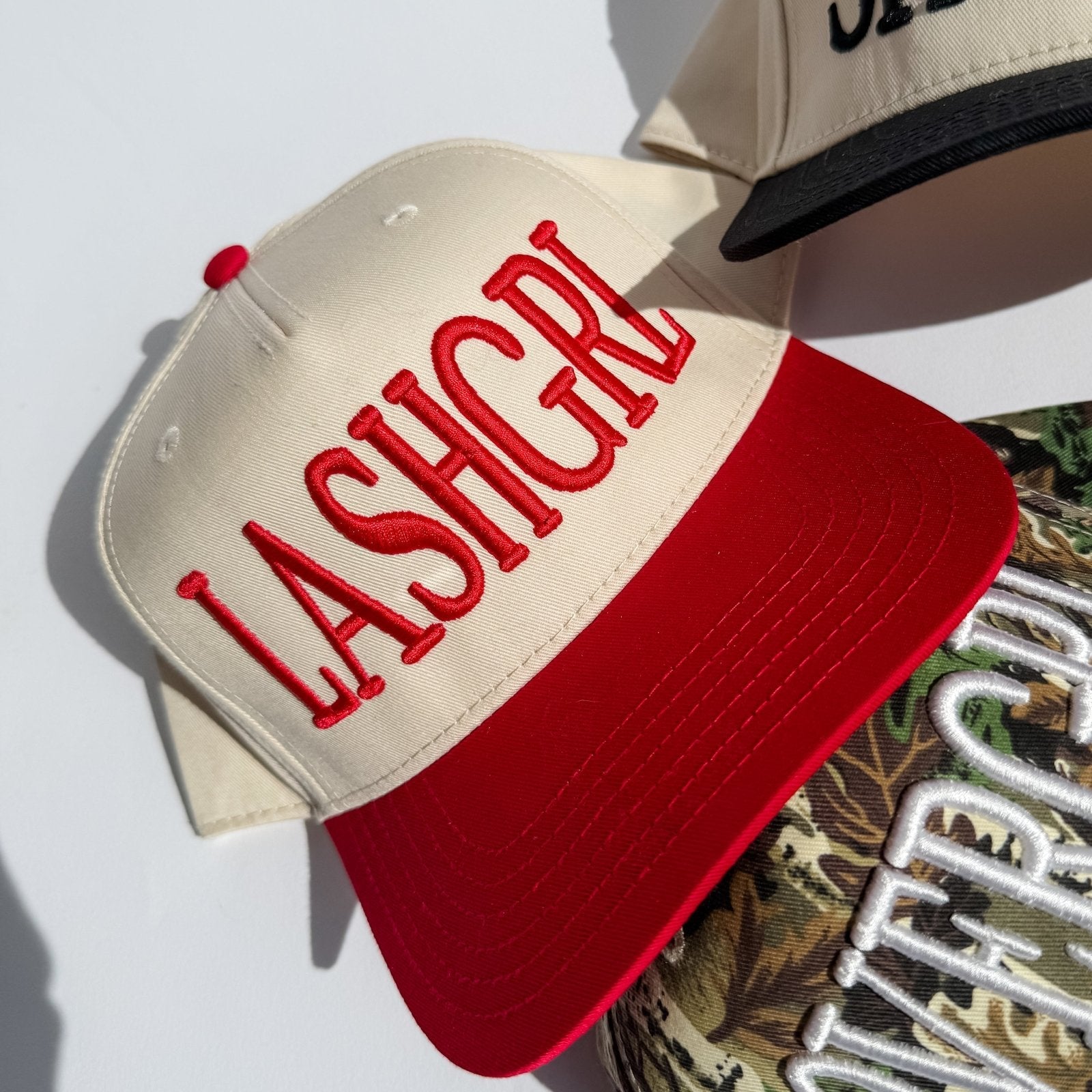 Cream trucker hat with red embroidered letters and red brim, angled view