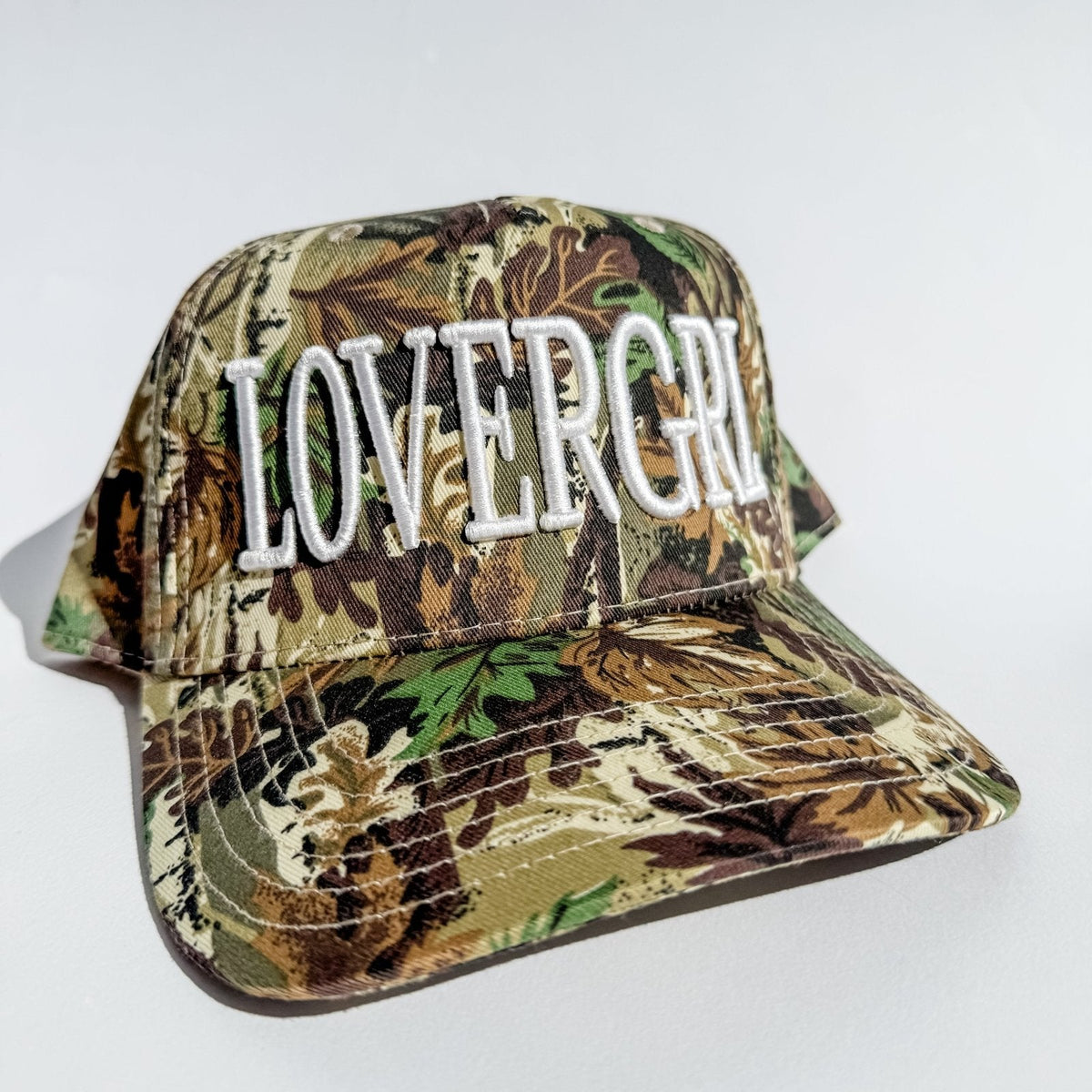 Camo trucker hat with embroidered 'LOVERGRL' letters on the front and curved brim