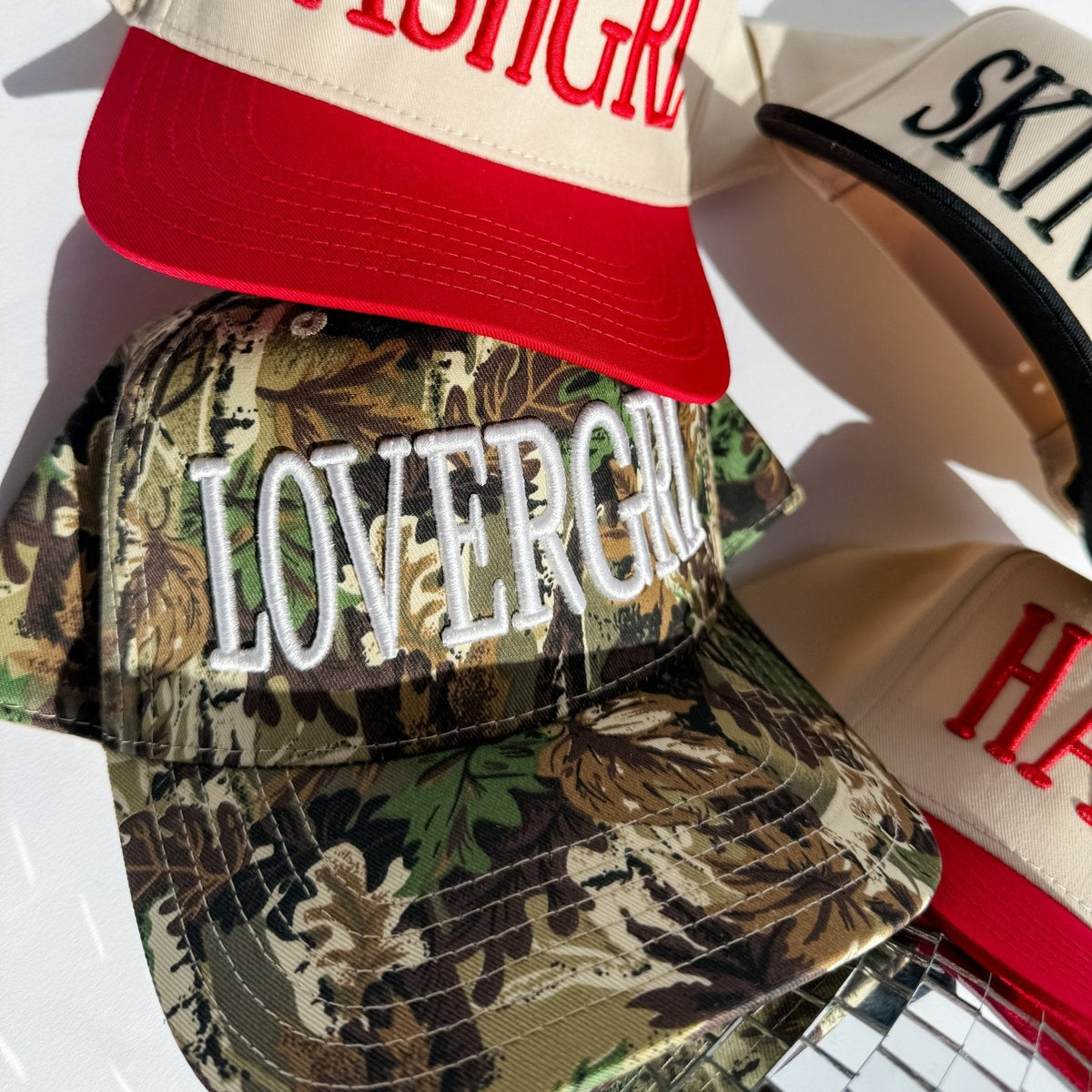 Camo trucker hat with embroidered 'LOVERGRL' logo front, curved brim, mesh back