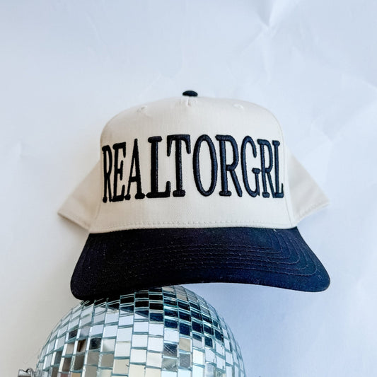 Cream and dark trucker hat with black “REALTORGRL” front lettering and curved brim